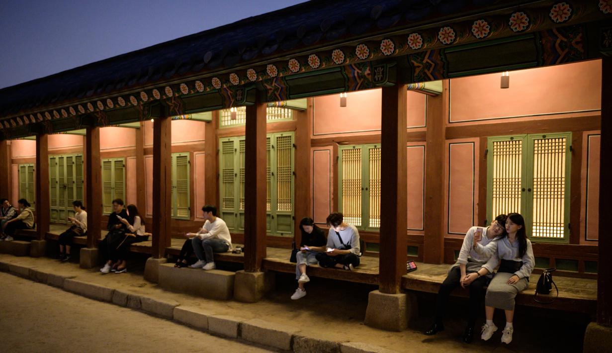 Gambar pada 4 Oktober 2019, wisatawan duduk di bangku dekat halaman saat kunjungan malam ke Istana Gyeongbokgung di Seoul, Korea Selatan. Kunjungan malam tersedia pada minggu ketiga dan keempat setiap bulan mulai dari 26 April sampai 31 Oktober, kecuali pada bulan Agustus. (Photo by Ed JONES / AFP)