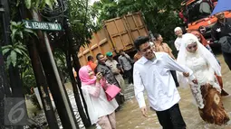 Pengantin Mansur dan Maya melintasi banjir usai melakukan akad nikah di KUA Mampang Prapatan, Jakarta, Selasa (21/2). Walaupun banjir sepasang pengantin ini tetap melakukan akad nikah. (Liputan6.com/Herman Zakharia)