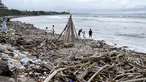 Orang-orang terlihat di samping tumpukan puing-puing dan sampah di di Pantai Kuta, Kabupaten Badung, Bali pada 26 Desember 2024. (SONNY TUMBELAKA/AFP)