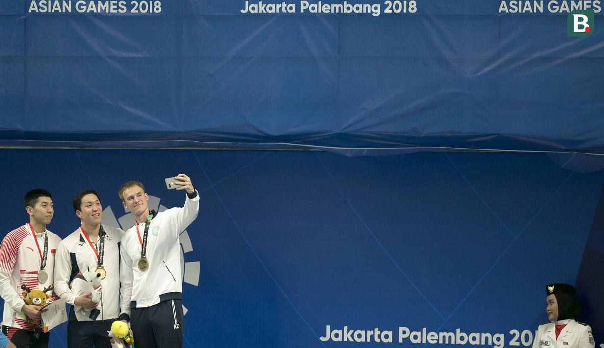 Dmitriy Balandin (kanan) mengajak wefie Yan Zibei asal China dan Yasuhiro Kozeki di podium usai final nomor 100 meter gaya dada putra pada Asian Games 2018 di Aquatik, GBK, Jakarta, Rabu (22/8/2018). (Bola.com/Peksi Cahyo)