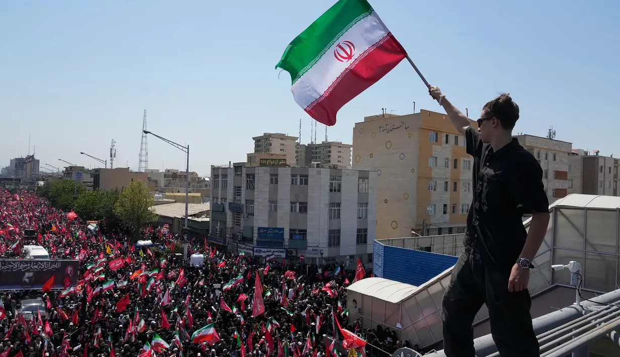 Seorang pria memegang bendera Iran saat truk yang membawa peti jenazah Pemimpin Tertinggi Iran Ayatollah Ali Khamenei dan anggota keluarganya yang terbunuh melintas  di Teheran, Iran, Senin, 6 Juli 2026. (AP Photo/Vahid Salemi)