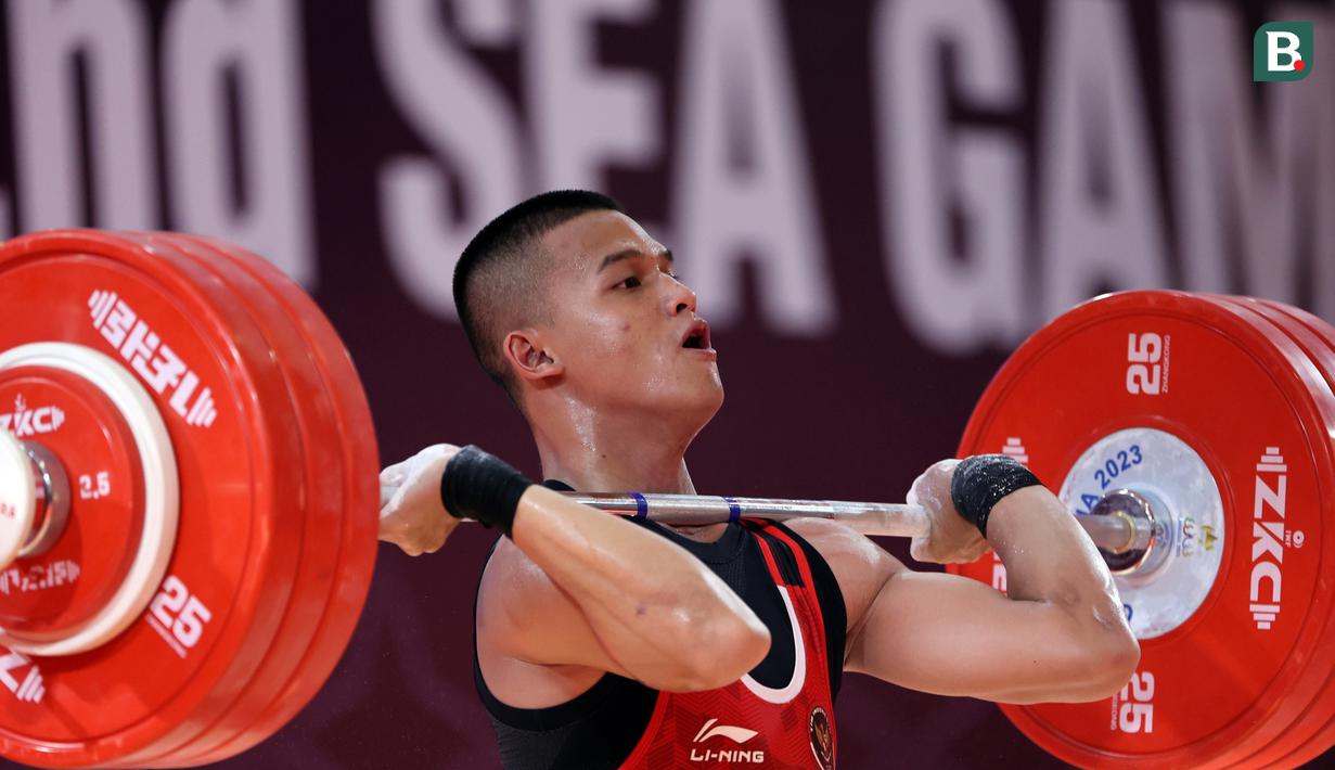 Atlet Indonesia, Rizki Juniansyah, berlaga pada cabang angkat besi 73 Kg putra SEA Games 2023 di Phnom Penh, Kamboja, Minggu (14/5/2022). Rizki tampil mengesankan dengan angkatan total 347 kg, terdiri dari 156 angkatan snatch dan 191 kg angkatan clean and jerk. (Bola.com/Abdul Aziz)
