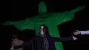 Seorang perempuan berpose di depan patung Kristus Penebus yang diterangi dengan warna hijau untuk memperingati Hari Lingkungan Hidup Sedunia, di Rio de Janeiro, Brasil, Senin, 5 Juni 2023. (AP Photo/Bruna Prado)