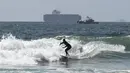 Peselancar melawan ombak di dekat dermaga di Huntington Beach, California (11/10/2021). Pantai Huntington membuka kembali garis pantainya setelah hasil pengujian air kembali dengan jumlah racun terkait minyak yang tidak terdeteksi di air laut. (Paul Bersebach/The Orange County Register via AP)