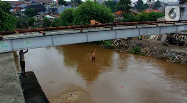 Seorang anak nekat melompat dari jembatan ke Kali Ciliwung Kalibata, Jakarta, Selasa (25/2/2020). Kali Ciliwung meluap usai hujan deras mengguyur Jakarta dan sekitarnya pada kemarin malam. (merdeka.com/magang/Muhammad Fayyadh)