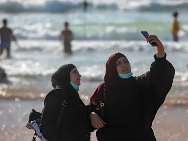 Wanita Palestina berselfie selama liburan Idul Fitri, di pantai laut Mediterania di Tel Aviv, Israel (25/5/2020).  Idul Fitri menandai akhir bulan suci Ramadhan, perayaan tiga hari yang biasanya menggembirakan telah berkurang secara signifikan karena pandemi coronavirus. (AP Photo/Oded Balilty)