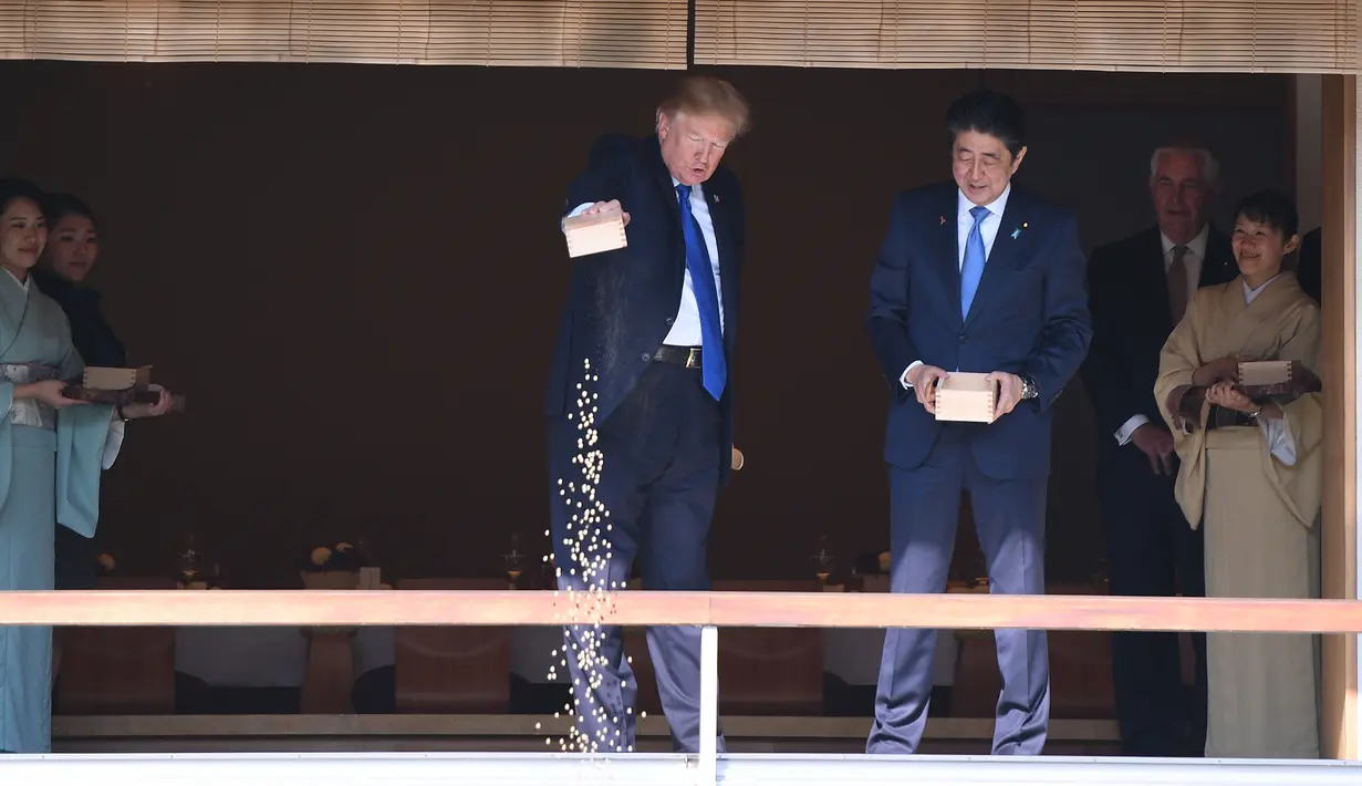 Presiden AS Donald Trump, disaksikan PM Jepang Shinzo Abe, menuangkan seluruh isi kotak makanan ikan ke kolam koi di Istana Akasaka, Tokyo, Senin (6/11). Tindakan Trump itu memicu kemarahan di kalangan pecinta ikan. (AFP PHOTO / TORU HANAI)