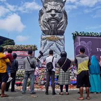 Orang-orang berdoa dekat patung singa, maskot Arema FC, di luar Stadion Kanjuruhan, Malang, Jawa Timur, Selasa (4/10/2022). Polri menjatuhkan sanksi kepada 10 anggota polisi dan menyelidiki 18 orang lainnya buntut tragedi kerusuhan yang menewaskan 125 orang di Stadion Kanjuruhan. (AP Photo/Dicky Bisinglasi)