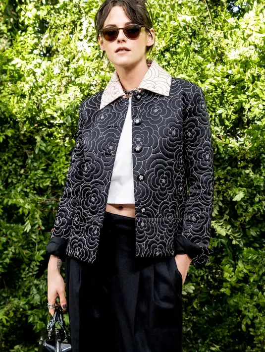 Hadir juga Kristen Stewart yang mengenakan jaket berkerah bunga hitam dan krem, atasan cropped putih dan celana panjang hitam. Bintang Twilight itu membawa tas Chanel berwarna hitam. [Dok/Chanel]
