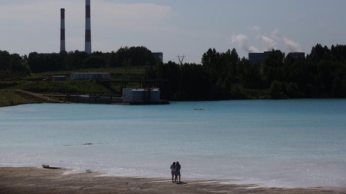 Pasangan berjalan dekat tempat pembuangan abu dari pabrik batubara lokal yang sering disebut 'Maladewa di Siberia' di Danau Novosibirsk, Rusia, Kamis (11/7/2019). Danau buatan yang memiliki hijau muda cerah tersebut kini tengah menjadi viral di media sosial Instagram. (Rostislav NETISOV/AFP)
