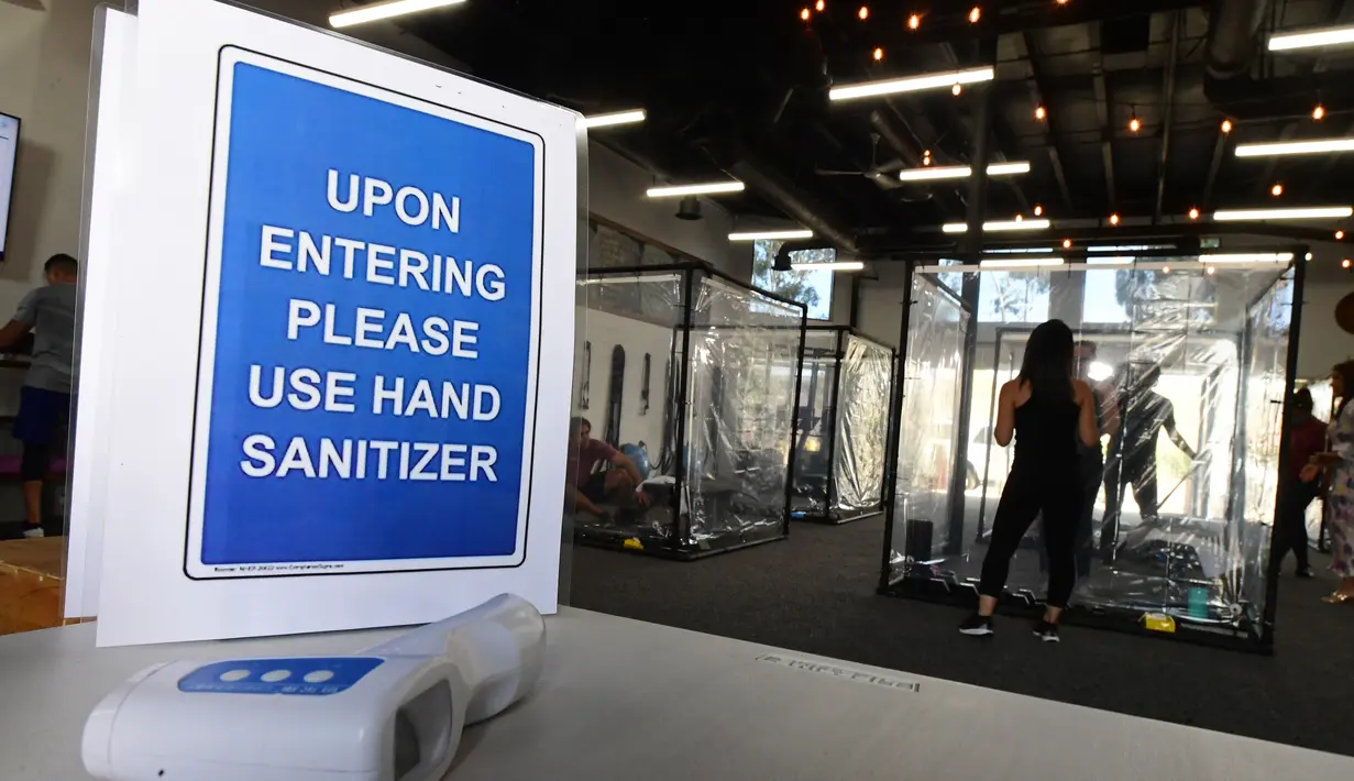 Sebuah tanda terlihat ketika orang-orang berolahraga dalam kotak plastik di Inspire South Bay Fitness di Redondo Beach, California pada 15 Juni 2020. Ruangan gym dengan plastik sebagai pemisah itu agar pengunjung dapat tetap berolahraga sambil tetap menjaga jarak fisik. (FREDERIC J. BROWN / AFP)