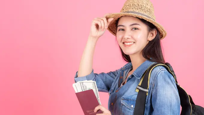 Seorang perempuan mengenakan pakaian berlibur dan memegang paspor (Foto Dok: Freepik/jcomp)