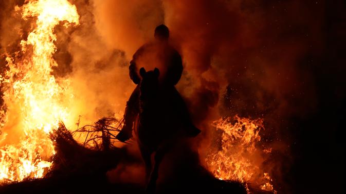 Seorang pria menunggangi kuda melewati api unggun saat festival Luminarias di San Bartolome de Pinares, Spanyol, Jumat (16/1/2020). Penduduk desa ini menegaskan tidak pernah ada warga maupun binatang yang terluka sepanjang festival diadakan. (AP Photo/Manu Fernandez)
