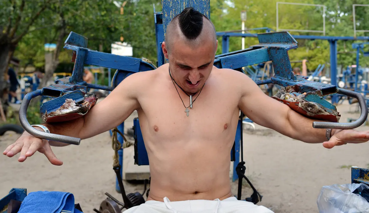 Valentyn (25) mengangkat beban saat berlatih fitnes di sebuah gym outdoor di Ibu Kota Ukraina, Kiev, 18 Agustus 2017. Alat olahraga di gym tersebut dibuat seorang teknisi bernama Yuri Kook pada dekade 1970-an. (GENYA SAVILOV/AFP)