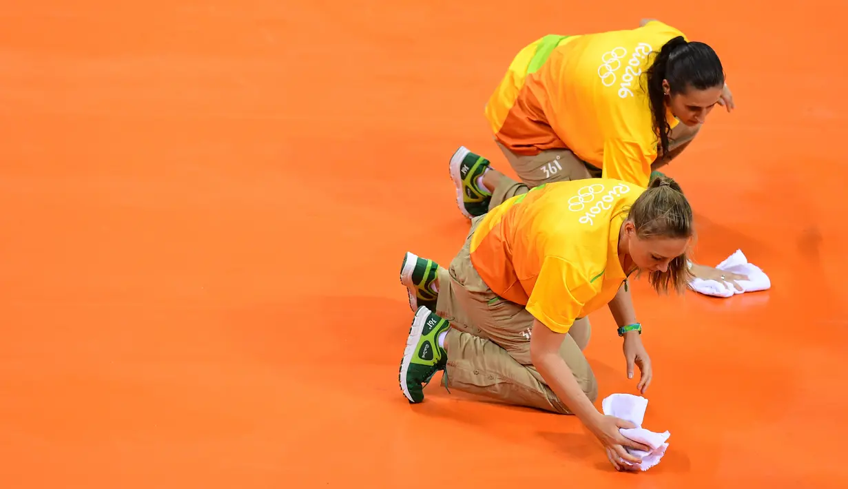 Dua orang relawan mengelap lapangan bola tangan sebelum dimulainya pertandingan cabang bola tangan putra Grup A Olimpiade 2016 antara Kroasia vs Qatar di Rio de Janeiro, 9 Agustus 2016. (AFP PHOTO/ Franck FIFE)