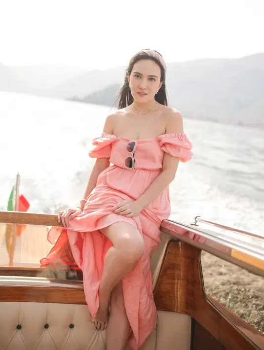 Berpose di kapal, Shandy Aulia kenakan long dress berwarna merah muda. Lengan pendek bersiluet balonnya diturunkan menjadi gaya off-the-shoulder. Foto: Instagram.