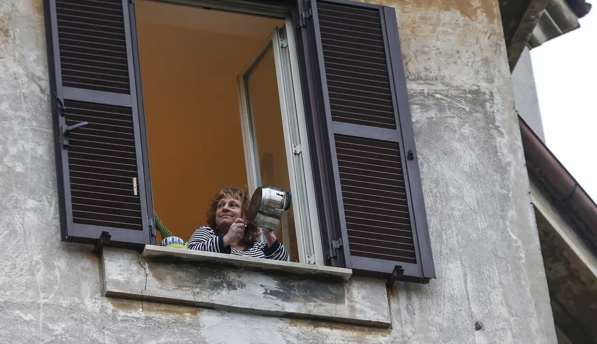 Seorang wanita bermain panci dari jendela rumah mereka selama flash mob di lingkungan Roma, Jumat (13/3/2020).  Lebih dari 23.000 orang berpartisipasi dalam flash mob untuk memainkan instrumen dan bernyanyi di tengah darurat virus corona Covid-19. (Cecilia Fabiano/LaPresse via AP)