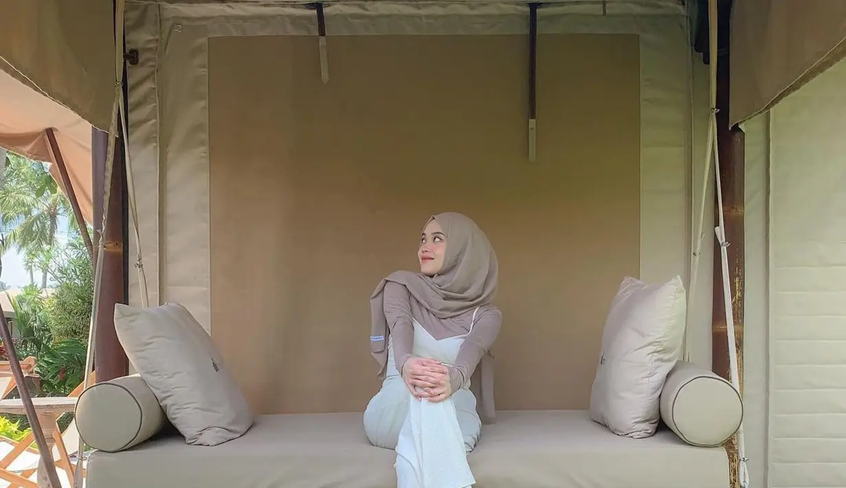 Beberapa jam sebelumnya, Putri Delina mengunggah pose tengah duduk sendirian di pendapa salah satu kamar Bali Beach Glamping dengan dinding warna pinggala yang kalem. Ia tampil santai bercelana panjang oversized kinantan yang dipadu dengan atasan turangga dan jilbab berwarna senada. Riasan yang natural membuat penampilannya makin cling. (Foto: Dok. Instagram @putridelinaa)