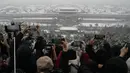Kerumunan orang dengan sepatu bot dan jaket mendaki bukit yang menghadap ke Kota Terlarang minggu ini untuk berdesak-desakan dengan orang lain yang mencoba mendapatkan gambar atap bekas istana kekaisaran yang tertutup salju. (AP Photo/Ng Han Guan)