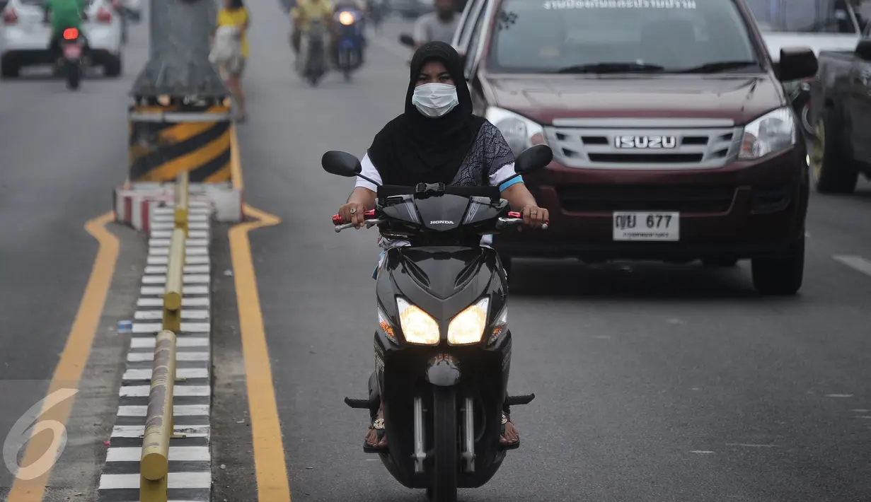 Seorang wanita mengenkaan masker saat mengendarai motor di Narathiwat yang diselimuti kabut, Thailand, Senin (5/10/2015). Kabut asap dari kebakaran hutan di Indonesia kini menyelimuti provinsi di wilayah selatan Thailand. (AFP PHOTO/Madaree TOHLALA)