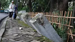Warga melintas di samping pagar yang ambruk di Taman Hutan Tebet, Jakarta, Kamis (28/3). Pagar yang ambruk tidak diperbaiki melainkan diganti menggunakan bambu. (Liputan6.com/Immanuel Antonius)