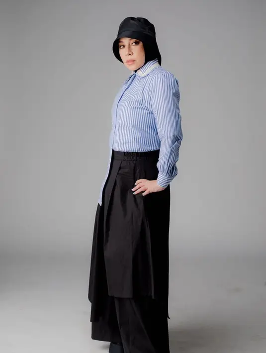 Seperti potret ini, Melly memadukan rok panjang, kemeja, serta bucket hat.