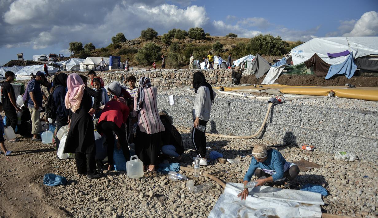 Para migran mengumpulkan air sementara yang lain membersihkan barang-barang mereka setelah hujan badai di kamp pengungsi Kara Tepe, di pulau Lesbos di timur laut Aegean, Yunani (14/10/2020).  (AP Photo/Panagiotis Balaskas)