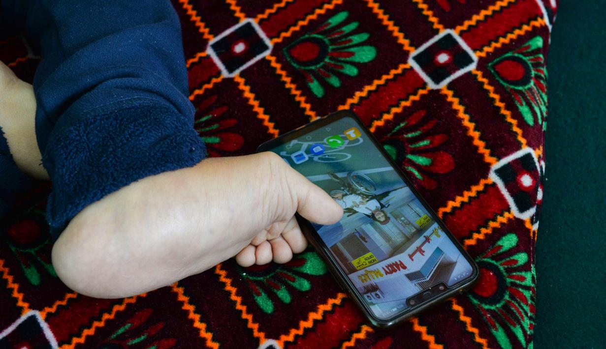 Seniman Robaba Mohammadi menggunakan ponsel dengan jari kaki di studionya di Kabul pada 5 Desember 2019. Meski terlahir dengan kaki dan tangan yang tidak bisa digunakan serta tak mendapatkan akses pendidikan, Robaba mampu membuat lukisan yang terbilang rumit dan penuh warna. (NOORULLAH SHIRZADA/AFP)