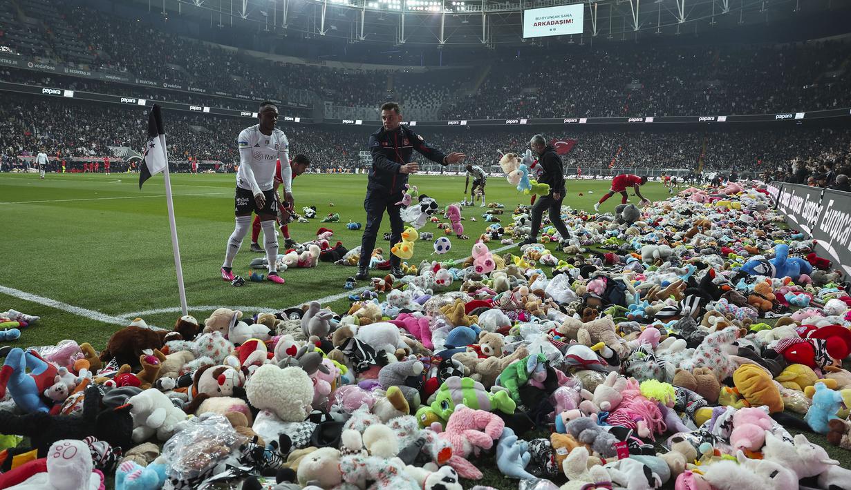 Pemain Besiktas dan Antalyaspor dibantu petugas mengumpulkan boneka yang dilemparkan oleh penonton pada laga lanjutan Liga Turki 2022/2023 yang berlangsung di Stadion Vodafone, Istanbul, Minggu (27/02/2023). Aksi tersebut ditujukan sebagai bentuk sumbangan untuk anak-anak korban gempa Turki. (AP Photo)
