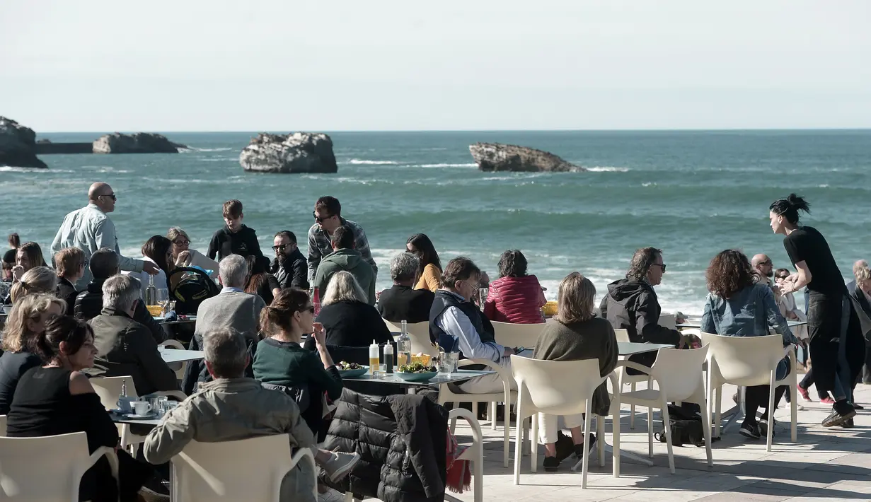Warga dan turis menikmati minuman di sebuah kafe selama cuaca musim dingin yang hangat di sepanjang garis pantai kota Biarritz di Perancis barat (17/2). Kota ini terletak di region Aquitane, Departemen Pyrénées-Atlantiques. (AFP Photo/Iroz Gaizka)