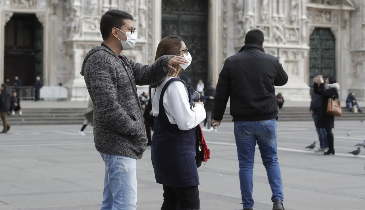 Suami istri mengenakan masker wajah berjalan-jalan di pusat kota Duomo, Milan, Italia, Kamis (27/2/2020). Pemerintah Italia akan melarang orang berciuman di tempat umum, berjabatan tangan dan menjaga jarak yang aman dari masing-masing lain untuk membatasi penyebaran virus corona. (AP Photo/Luca Brun