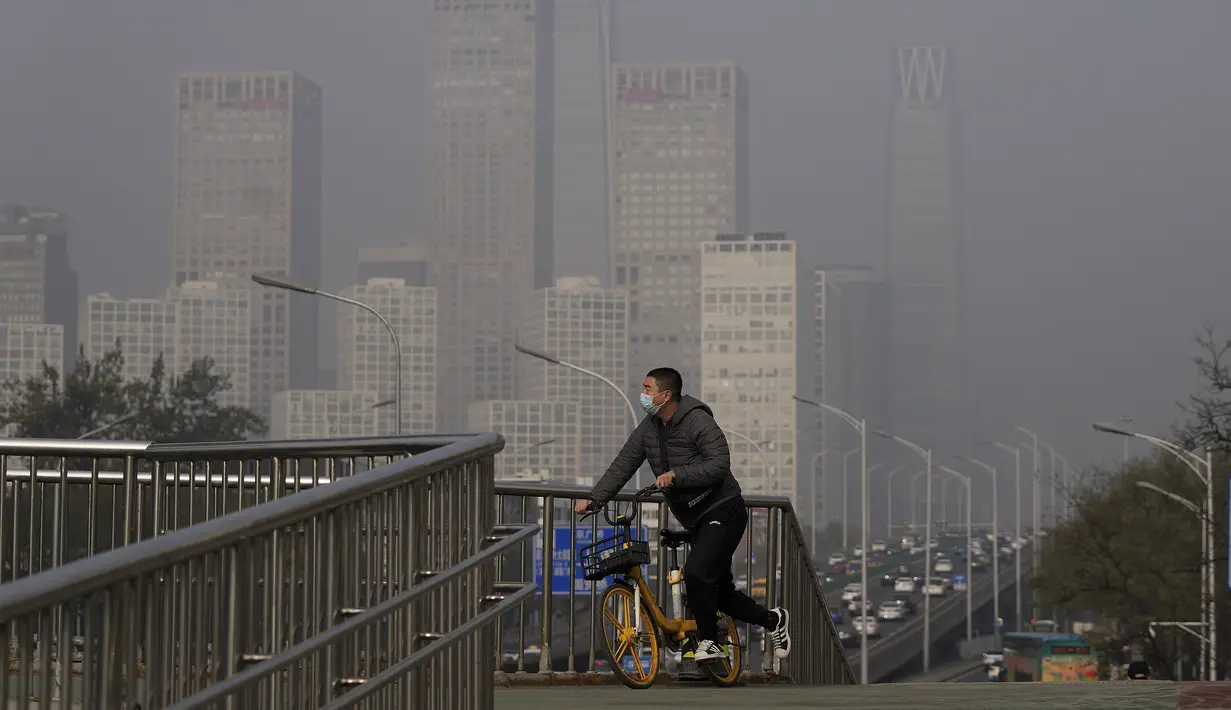 Seorang pria yang mengenakan masker untuk membantu mengekang penyebaran virus corona mengendarai sepeda di jembatan di atas gedung perkantoran di Central Business District yang diselimuti kabut polusi di Beijing, Kamis (18/11/2021).  (AP Photo/Andy Wong)