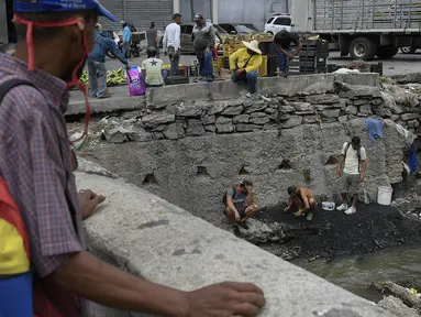 Pria mencari potongan tembaga, emas atau perak untuk dijual di tengah pandemi virus corona baru di Sungai Guaire yang tercemar, di lingkungan Quinta Crespo di Caracas, Venezuela (19/1/2021). Krisis ekonomi Venezuela telah mengirim jutaan orang melarikan diri. (AP Photo/Matias Delacroix)