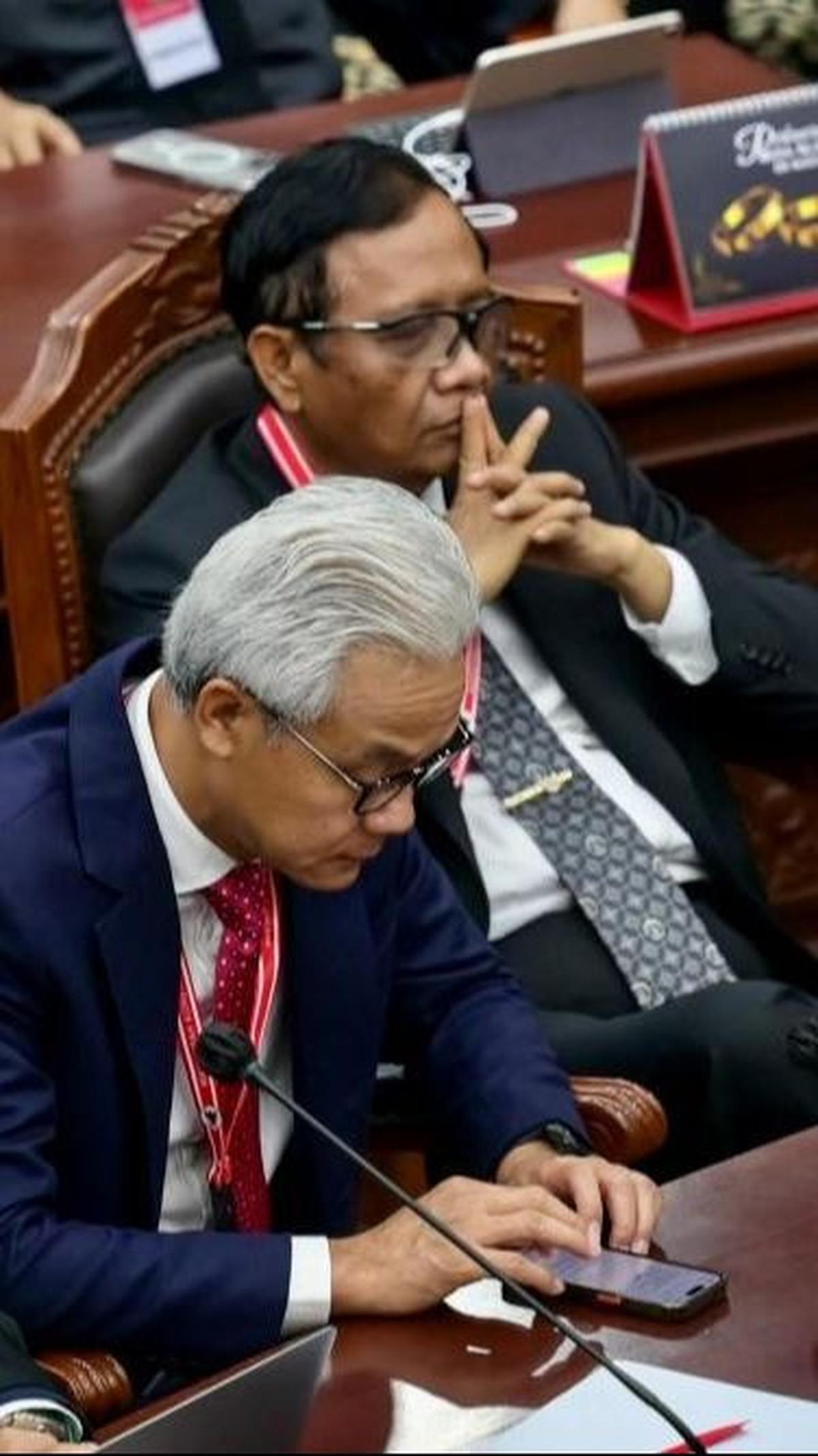 Ganjar juga sempat sibuk dengan ponselnya ketika sidang putusan tersebut sedang berlangsung. Sementara Mahfud duduk bersandar di kursi sambil mengangkat kedua tangannya ke depan bibirnya.&nbsp;Foto: AFP