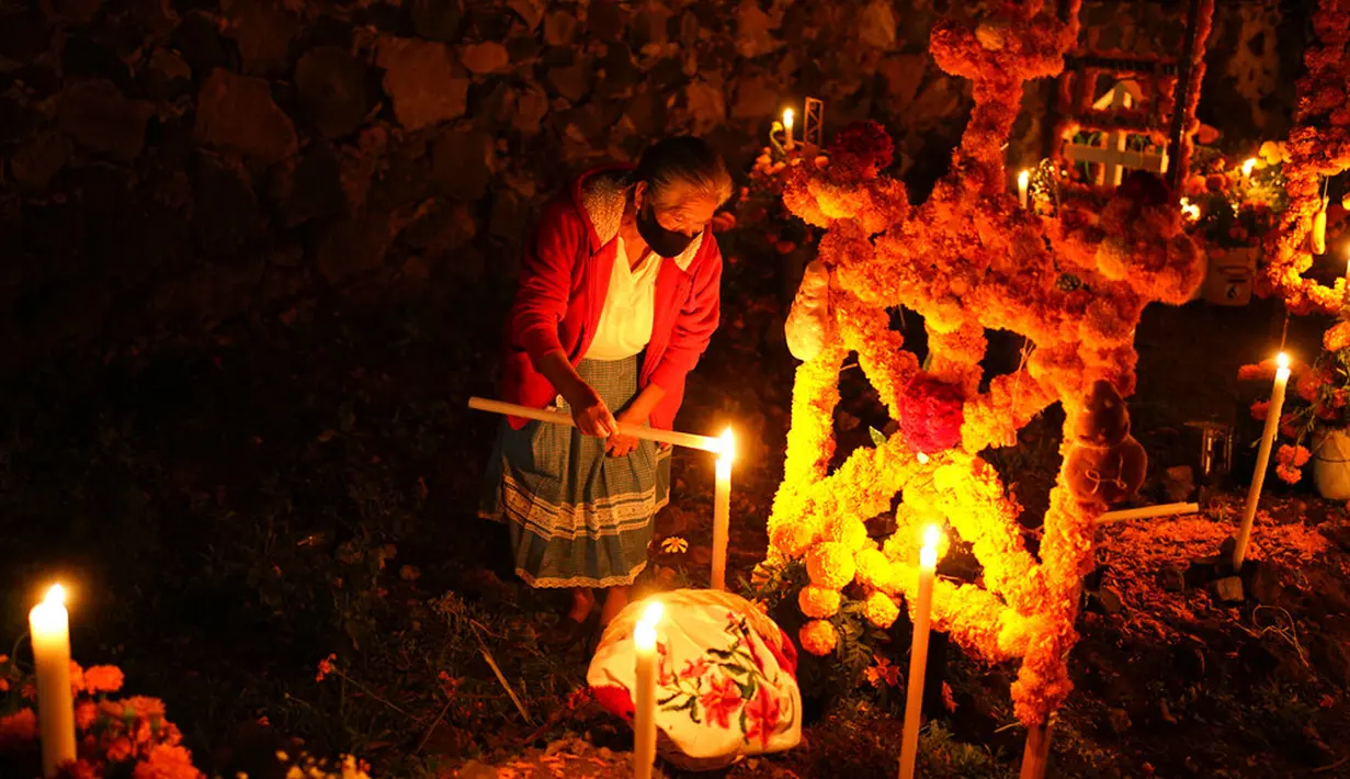 Seorang wanita menyalakan lilin di sebelah makam orang yang dicintainya pada perayaan Hari Kematian di pemakaman Arocutin, Michoacan, Meksiko, 1 November 2021. Pada Hari Kematian, kerabat menghabiskan malam di samping makam orang yang mereka cintai. (AP Photo/Eduardo Verdugo)