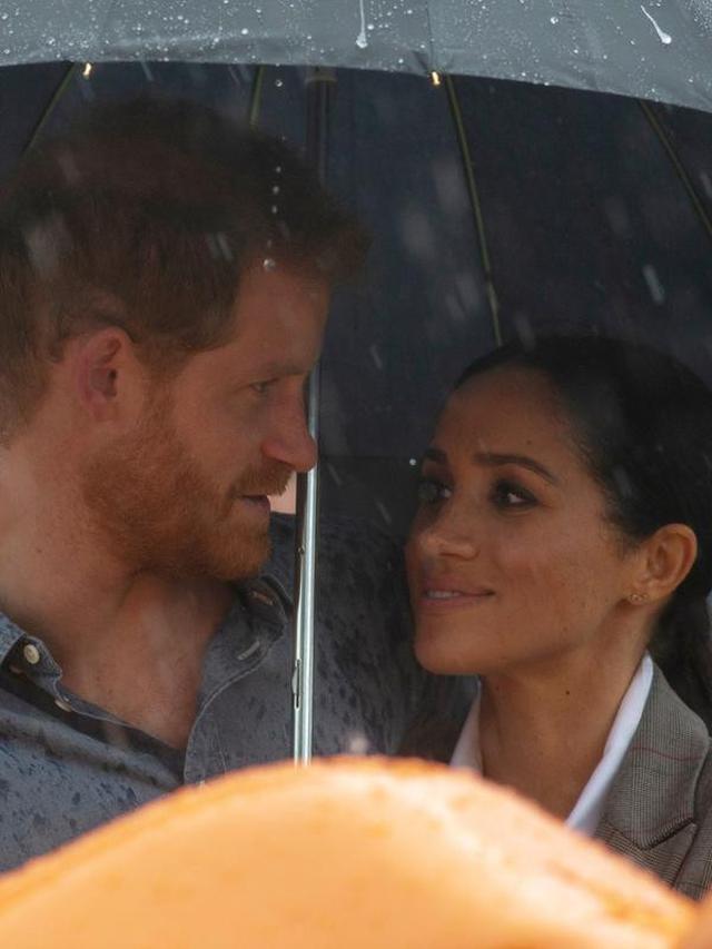 Pangeran Harry dan Meghan Markle berlindung di bawah payung saat piknik di Victoria Park, Dubbo, Australia, Rabu (17/10). Ini adalah hari kedua Pangeran Harry dan Meghan Markle dalam kunjungannya ke Australia. (Ian Vogler/Pool via AP)