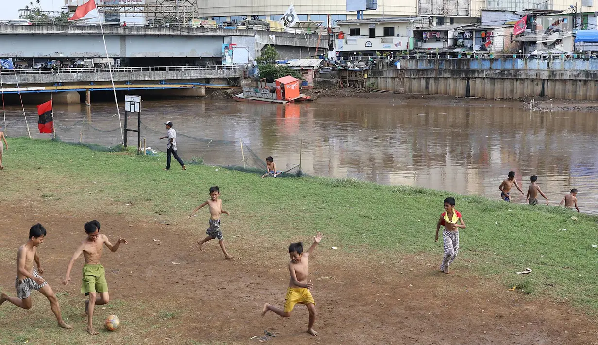 Anak-anak bermain sepak bola di bantaran Kanal Banjir Barat, Jakarta, Jumat (5/4). Tidak adanya lapangan menjadikan lokasi tersebut sebagai tempat bermain mereka, meskipun dalam kondisi seadanya. (Liputan6.com/Immanuel Antonius)