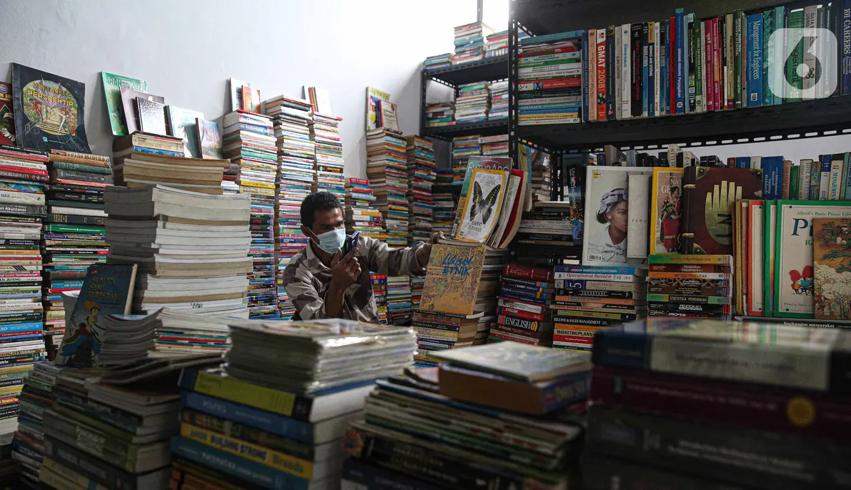 Pedagang bermain ponsel saat menunggu pembeli buku di Pasar Kenari, Jakarta, Rabu (24/11/2021). Semua toko yang berada di lantai 3 merupakan toko subsidi dari pemerintah.  (Liputan6.com/Faizal Fanani)