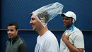Seorang penonton melindungi kepalanya dengan plastik menunggu penundaan pertandingan akibat hujan selama putaran pertama turnamen tenis AS Terbuka 2017 di New York (29/8). (AP Photo / Andres Kudacki)