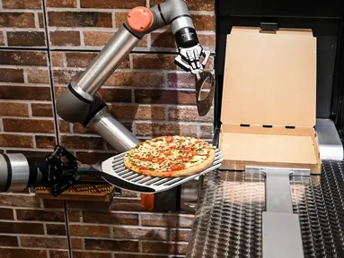 Foto yang diambil pada 1 Juli 2021 menunjukkan "Pazzi", robot pembuat pizza yang sedang bekerja di sebuah restoran di Paris. Robot pembuat pizza dari startup Paris Pazzi tersebut mulai beroperasi di jantung kota Paris pada 5 Juli 2021 (BERTRAND GUAY/AFP)