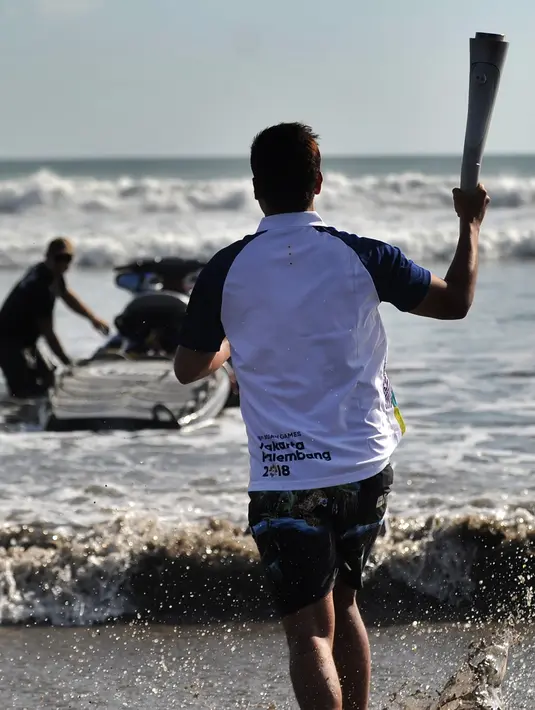 Aktor Hamish Daud (kedua kiri) membawa obor pada kirab obor Asian Games 2018 di Pantai Kuta, Bali, Senin (23/7). Torch Relay Asian Games 2018 melintasi empat kabupaten di Bali dengan arak-arakan berkeliling di sejumlah obyek wisata. (AFP/SONNY TUMBELAKA)