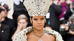 Penyanyi Rihanna berpose untuk fofotgrafer setibanya pada pagelaran Met Gala 2018 di Museum Seni Metropolitan New York, Senin (7/5). Menyempurnakan gayanya, aksesori di kepalanya yang menyerupai mitre atau mitra. (Charles Sykes/Invision/AP)