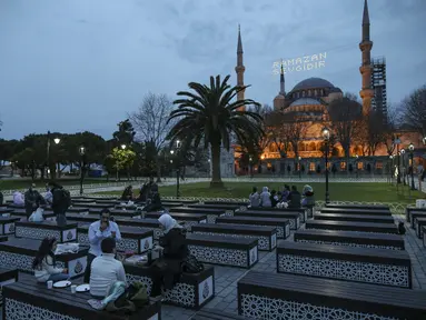 Orang-orang berbuka puasa dengan latar belakang Masjid Sultan Ahmed yang ikonik, lebih dikenal sebagai Masjid Biru, dihiasi dengan lampu dan slogan bertuliskan "Ramadhan adalah cinta," menandai bulan Ramadhan, di distrik bersejarah Sultan Ahmed di Istanbul (13/4/2021). (AP Photo/Emrah Gurel)