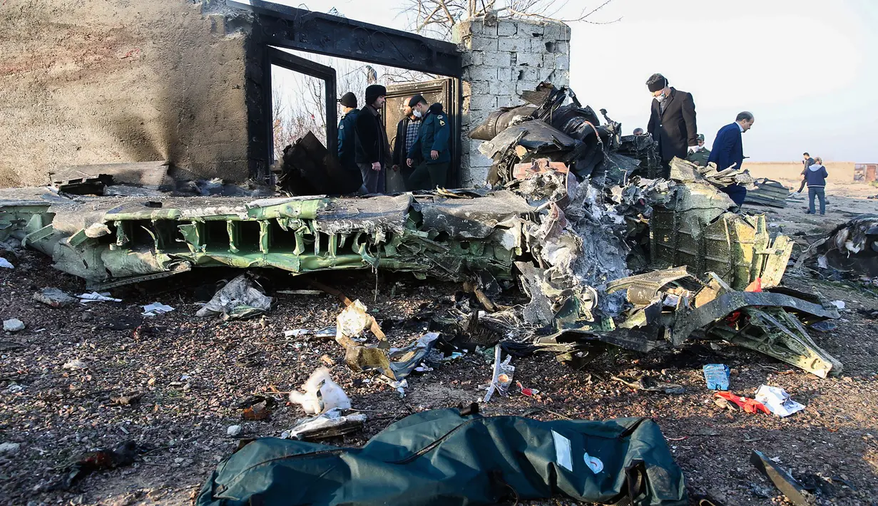 Orang-orang berdiri di antara puing-puing setelah pesawat Boeing 737 jatuh di dekat Bandara Internasional, Teheran, Iran, Rabu (8/1/2020). Seluruh penumpang pesawat maskapai Ukraina yang membawa 176 orang termasuk kru tersebut dilaporkan tewas. (ROHHOLLAH VADATI / ISNA / AFP)