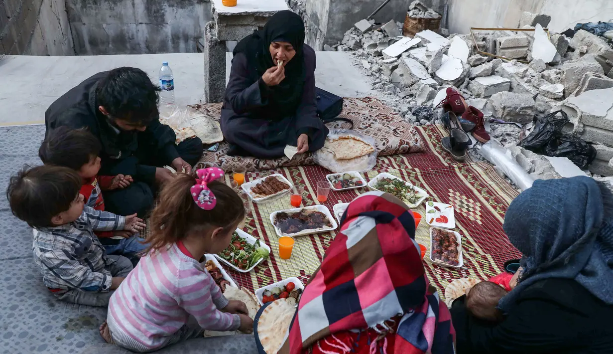 Keluarga Tareq Abu Ziad berbuka puasa di tengah reruntuhan rumah mereka yang hancur setelah serangan militer pasukan pemerintah dan sekutunya di Kota Ariha, Provinsi Idlib, Suriah, Senin (4/5/2020). Muslim Suriah melewati Ramadan tahun ini masih dalam kondisi perang. (AAREF WATAD/AFP)