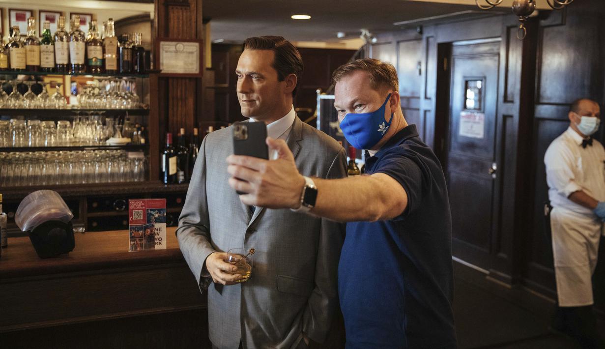 Steve Tukavkin (kanan) berswafoto dengan patung lilin aktor John Hamm di Peter Luger Steakhouse, New York, Jumat (26/2/2021). Patung yang dipinjam dari Madame Tussauds tersebut membantu mengisi meja kosong selama pelonggaran pembatasan aturan COVID-19 makan di dalam ruangan.  (AP Photo/Kevin Hagen)