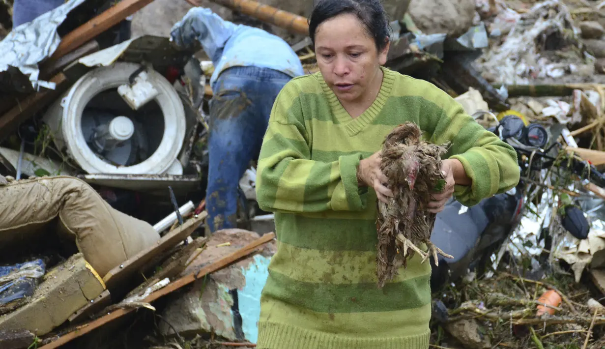 Seorang wanita membawa ayam hidup dari puing-puing setelah lereng bukit yang diguyur hujan runtuh menimpa rumah-rumah di Pereira, Kolombia, Selasa (8/2/2022). Hujan deras memicu tanah longsor yang menyapu daerah perumahan ini, menewaskan sedikitnya 14 orang dan melukai 35 lainnya. (AP Photo/Andres O