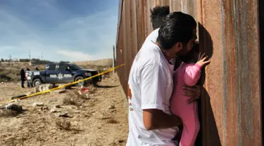 Seorang pria sambil menggendong bayi melepas rindu dengan kerabat dalam acara "Keep our dream alive" di dinding perbatasan antara Meksiko dan Amerika Serikat di Ciudad Juarez, negara bagian Chihuahua, 10 Desember 2017. (Herika MARTINEZ/AFP)