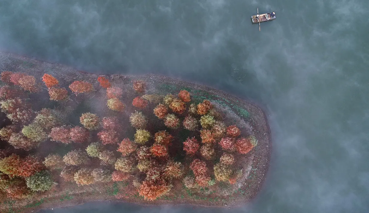 Warga mengendarai perahu di Danau Tianquan yang berselimut kabut di Xuyi di Provinsi Jiangsu, China (20/11/2019). Memasuki musik dingin, pemandangan Danau Tianquan berselimut kabut tipis berpadu dengan pepohonan berdaun kemerahan terlihat lebih indah dari biasanya. (AFP Photo/Str)