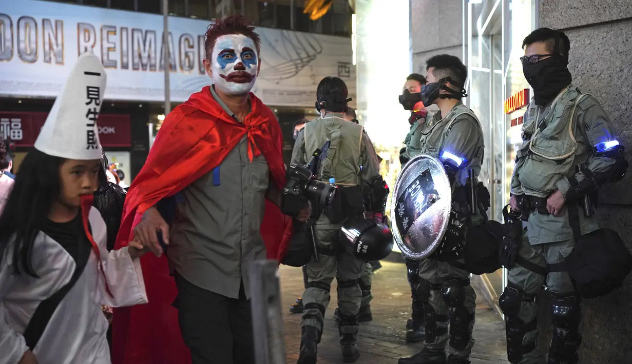 Seorang pria dengan kostum Halloween berjalan melewati petugas polisi dengan pakaian anti huru hara di Hong Kong, Kamis (31/10/2019). Polisi Hong Kong bersiap untuk berjaga unjuk rasa Kamis malam, yang akan menguji peraturan larangan pemerintah untuk menutup wajah yang diperkenalkan bulan ini. (AP P
